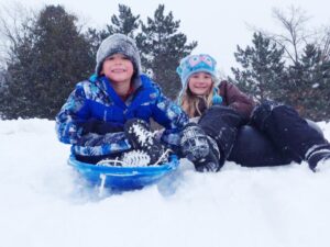 2 children sit on their sleds in the snow