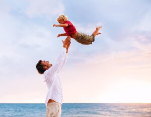 Man Tosses small child in the air, ocean background